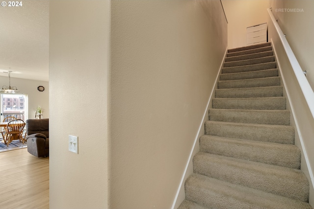 stairs featuring wood-type flooring and a chandelier