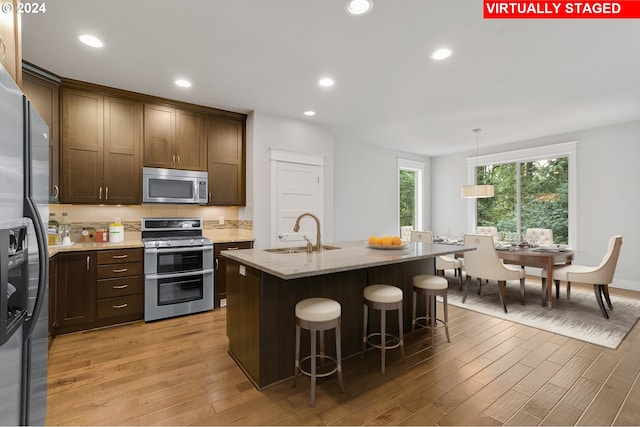 kitchen featuring a center island with sink, sink, hanging light fixtures, light wood-type flooring, and appliances with stainless steel finishes