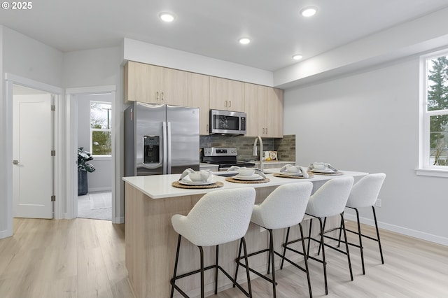 kitchen featuring light brown cabinets, stainless steel appliances, backsplash, light hardwood / wood-style flooring, and a breakfast bar area