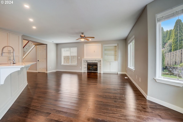 unfurnished living room featuring ceiling fan, sink, dark wood-type flooring, and built in shelves