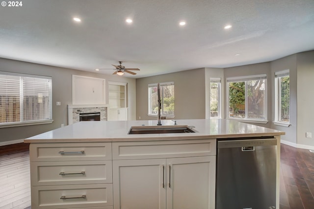 kitchen with sink, dark wood-type flooring, stainless steel dishwasher, a fireplace, and white cabinets