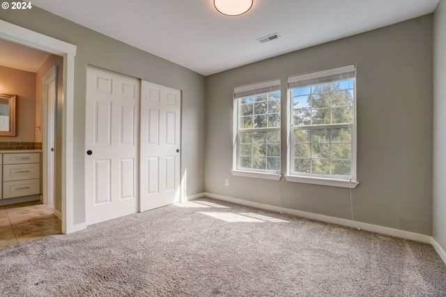 unfurnished bedroom with connected bathroom, light carpet, and a closet