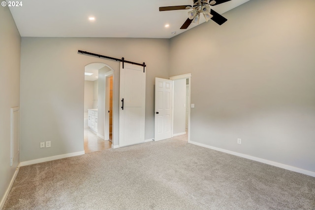 carpeted spare room featuring ceiling fan, a barn door, and high vaulted ceiling