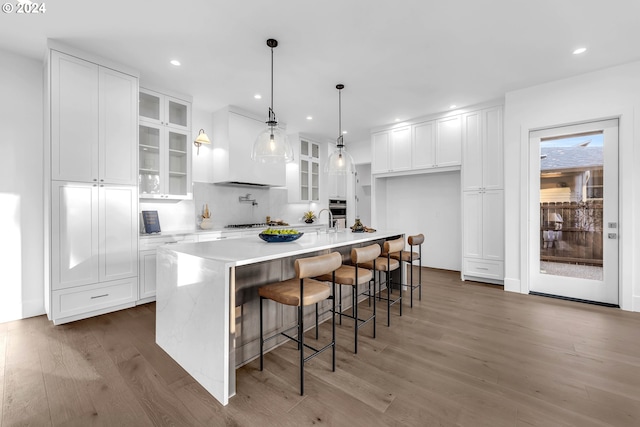 kitchen featuring dark hardwood / wood-style floors, a kitchen bar, hanging light fixtures, an island with sink, and white cabinetry