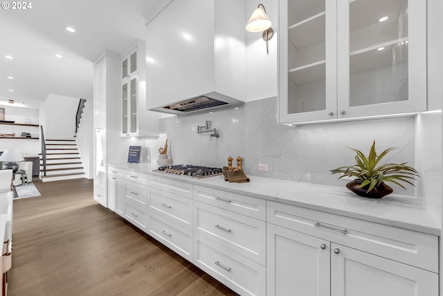 kitchen with light stone counters, white cabinets, custom exhaust hood, stainless steel gas cooktop, and dark hardwood / wood-style flooring