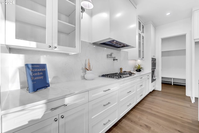 kitchen featuring white cabinets, appliances with stainless steel finishes, premium range hood, and light wood-type flooring