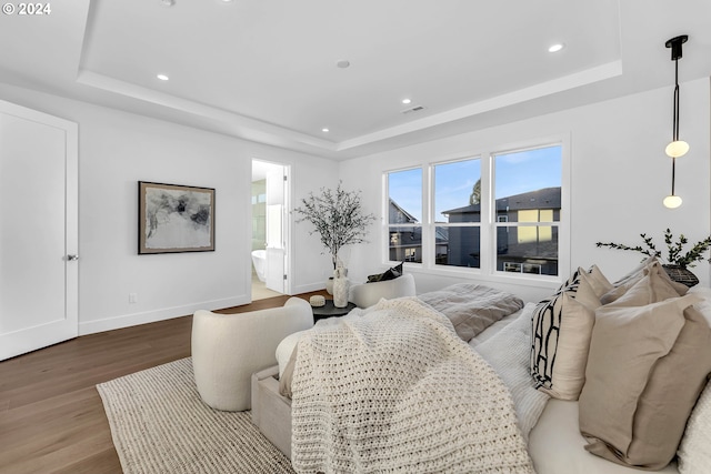 bedroom featuring wood-type flooring, a tray ceiling, and ensuite bathroom