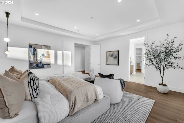 bedroom featuring wood-type flooring, a tray ceiling, and ensuite bath