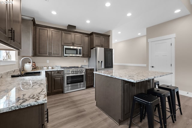 kitchen featuring appliances with stainless steel finishes, sink, a kitchen island, light hardwood / wood-style floors, and light stone counters