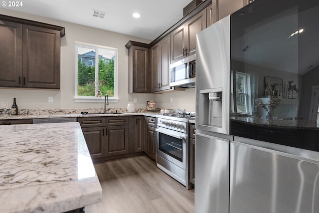 kitchen featuring stainless steel appliances, sink, light stone countertops, dark brown cabinetry, and light wood-type flooring