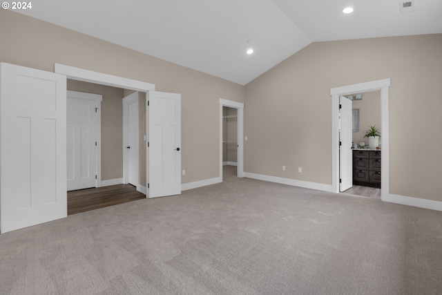 unfurnished bedroom with connected bathroom, light carpet, a spacious closet, and lofted ceiling