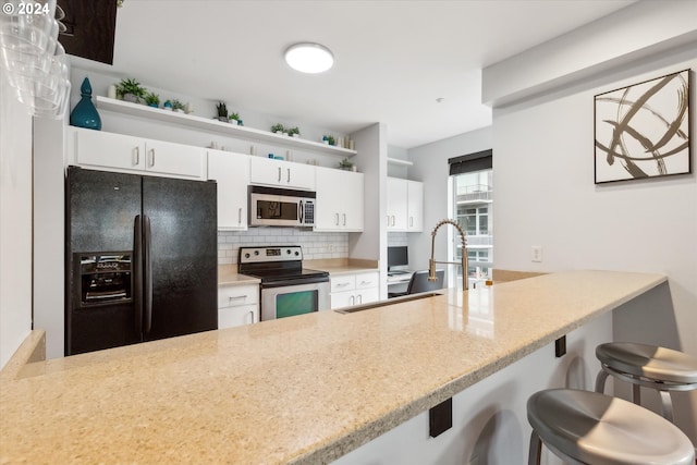 kitchen featuring appliances with stainless steel finishes, white cabinetry, a kitchen breakfast bar, and tasteful backsplash