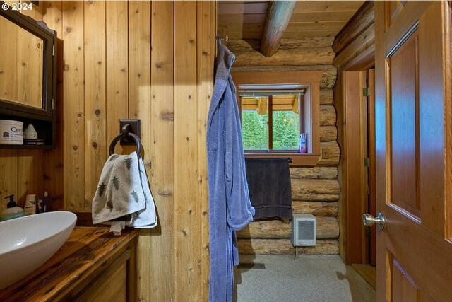 bathroom with wood ceiling, rustic walls, beamed ceiling, and vanity