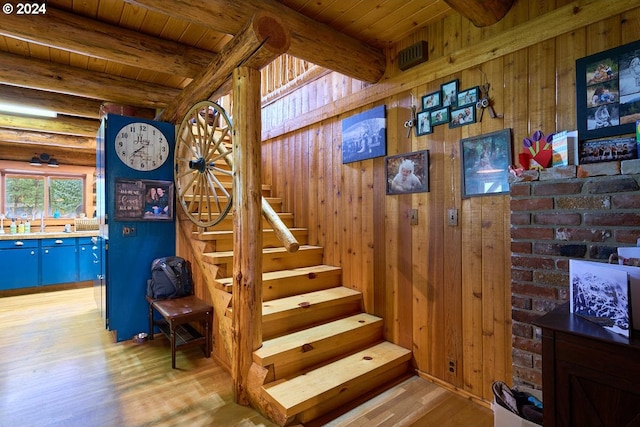 staircase with hardwood / wood-style floors, log walls, wood ceiling, wood walls, and beam ceiling