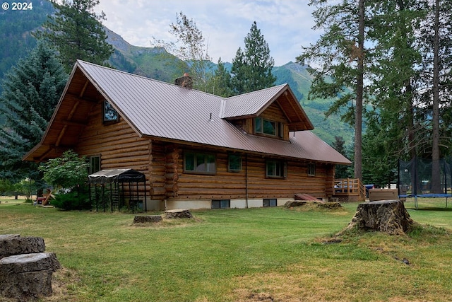 rear view of property with a mountain view, a lawn, and a trampoline