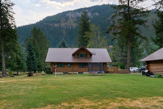 back of property featuring a yard, a deck with mountain view, and a trampoline