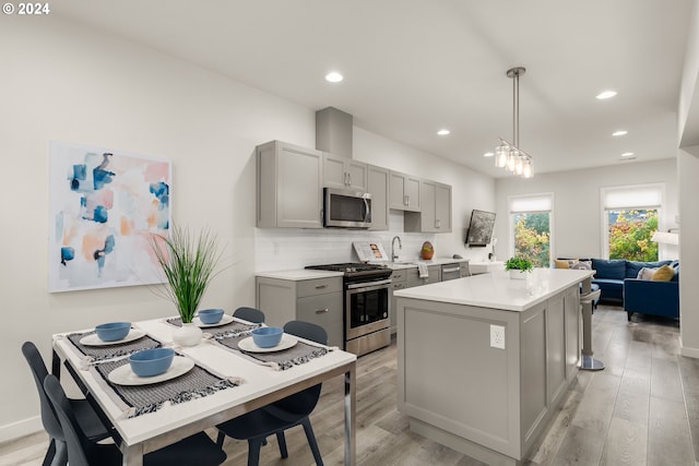 kitchen featuring a center island, light wood-type flooring, appliances with stainless steel finishes, decorative backsplash, and gray cabinets