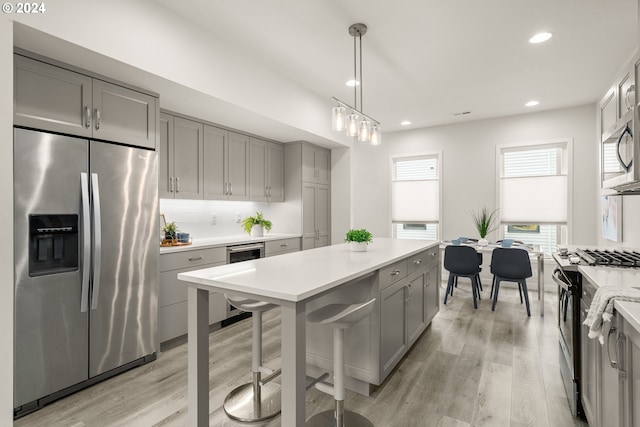 kitchen featuring light wood-type flooring, gray cabinets, hanging light fixtures, beverage cooler, and stainless steel appliances