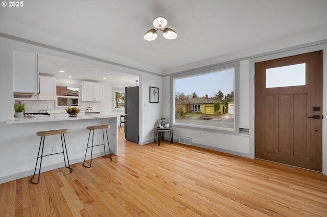 kitchen with a kitchen breakfast bar, light hardwood / wood-style floors, stainless steel fridge, white cabinetry, and kitchen peninsula