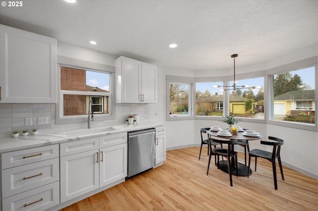 kitchen featuring white cabinetry, light wood-type flooring, decorative light fixtures, sink, and stainless steel dishwasher