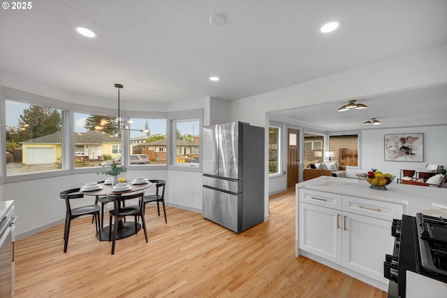 kitchen with white cabinetry, range, hanging light fixtures, stainless steel refrigerator, and light hardwood / wood-style floors