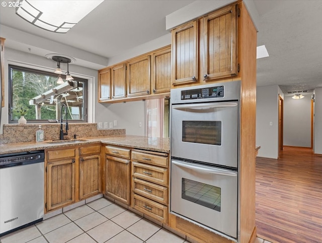 kitchen with pendant lighting, sink, light hardwood / wood-style flooring, appliances with stainless steel finishes, and a skylight