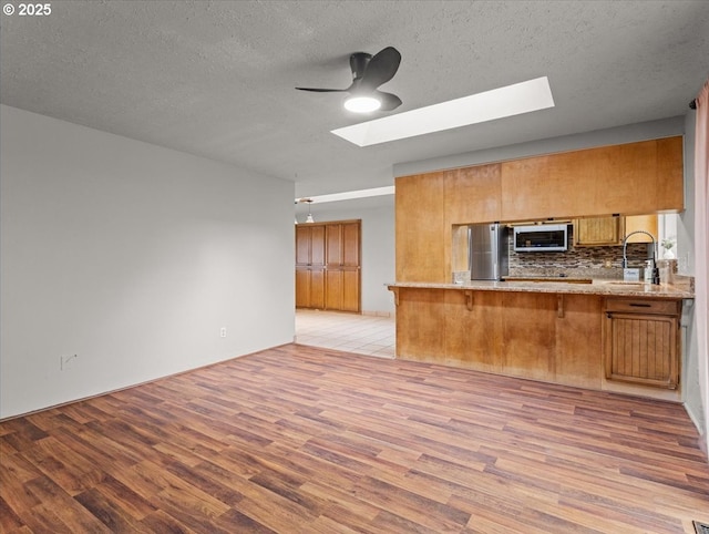 kitchen with light hardwood / wood-style flooring, appliances with stainless steel finishes, backsplash, a skylight, and kitchen peninsula