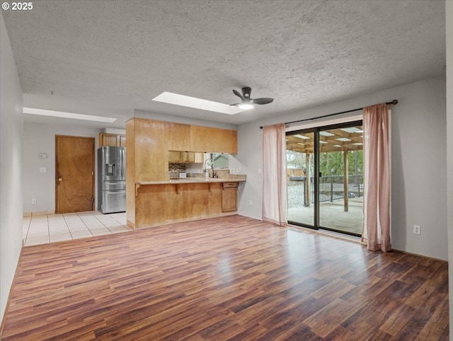 unfurnished living room with sink, a skylight, ceiling fan, and light wood-type flooring