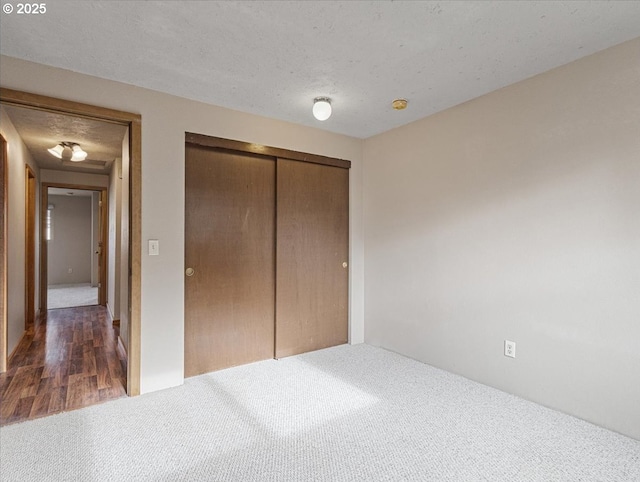 unfurnished bedroom featuring dark carpet, a textured ceiling, and a closet