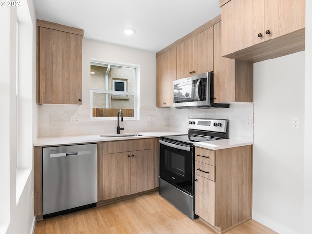 kitchen featuring appliances with stainless steel finishes, tasteful backsplash, sink, light wood-type flooring, and light brown cabinetry