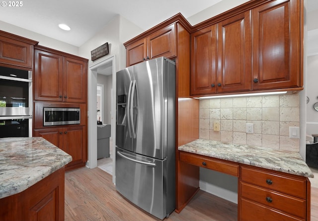 kitchen with light stone counters, decorative backsplash, stainless steel appliances, and light wood-type flooring