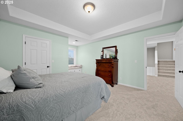 bedroom featuring light colored carpet, a tray ceiling, and a textured ceiling