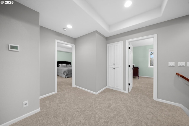 hallway featuring light carpet and a tray ceiling