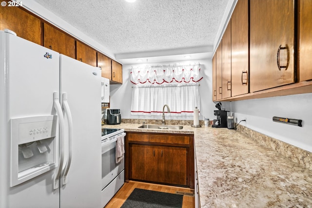 kitchen with stainless steel stove, sink, white refrigerator with ice dispenser, a textured ceiling, and light hardwood / wood-style floors