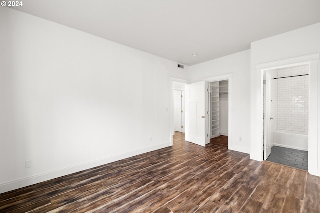 unfurnished bedroom with ensuite bathroom, dark wood-type flooring, and a closet