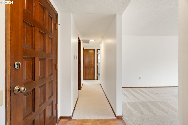 hall with light colored carpet and a textured ceiling