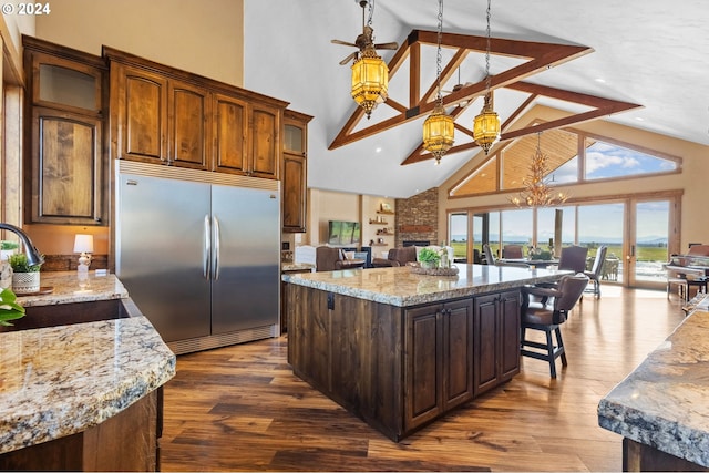 kitchen with stainless steel built in refrigerator, high vaulted ceiling, a kitchen island, and sink