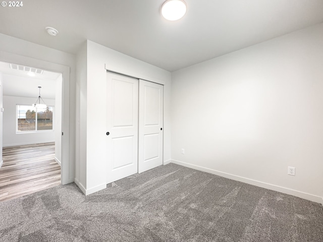 unfurnished bedroom with carpet flooring, a chandelier, and a closet