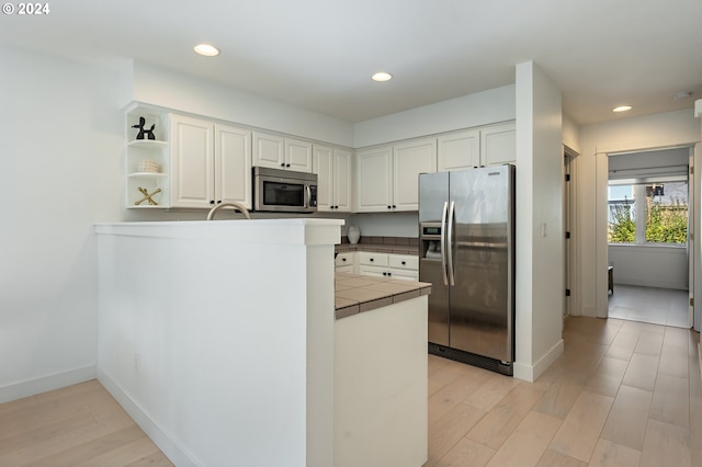 kitchen with appliances with stainless steel finishes, light hardwood / wood-style floors, white cabinetry, kitchen peninsula, and tile countertops