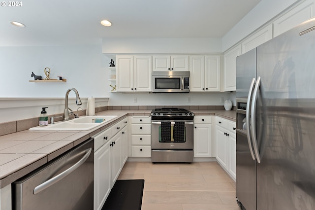 kitchen featuring appliances with stainless steel finishes, white cabinets, light hardwood / wood-style flooring, tile counters, and sink