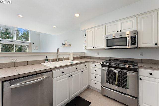 kitchen with appliances with stainless steel finishes, white cabinetry, light wood-type flooring, tile counters, and sink