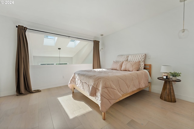 bedroom featuring lofted ceiling with skylight and light hardwood / wood-style flooring