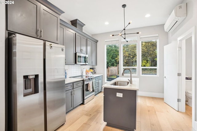 kitchen featuring sink, light wood-type flooring, appliances with stainless steel finishes, a wall mounted AC, and decorative light fixtures