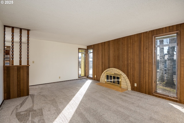 unfurnished living room featuring a fireplace, carpet, a textured ceiling, and wood walls