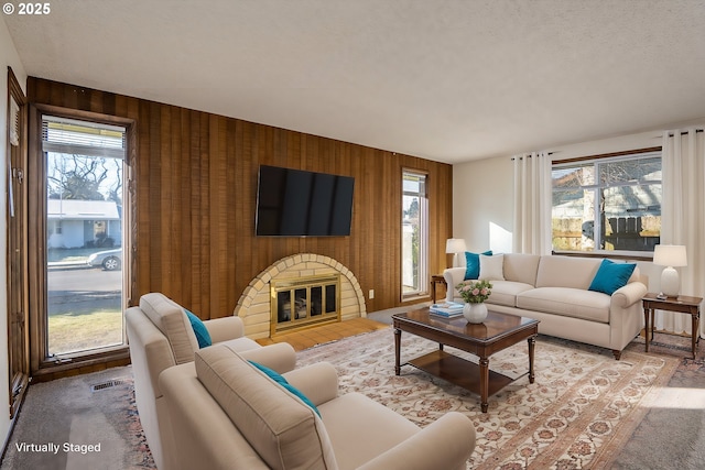 living room featuring plenty of natural light, wooden walls, and a brick fireplace