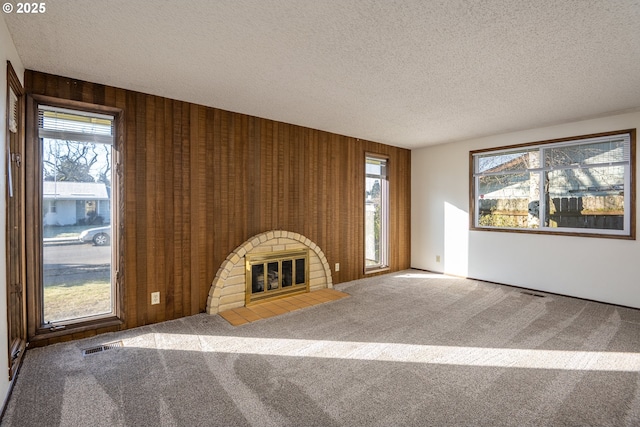 unfurnished living room with carpet flooring, a wealth of natural light, a textured ceiling, and a fireplace