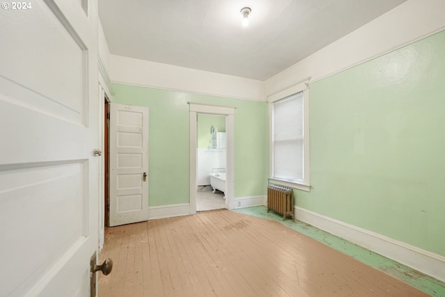 unfurnished bedroom featuring ensuite bathroom, radiator, and hardwood / wood-style flooring