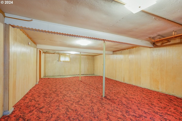 basement featuring wooden walls, a textured ceiling, and carpet floors