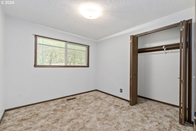 unfurnished bedroom featuring light carpet, a textured ceiling, and a closet