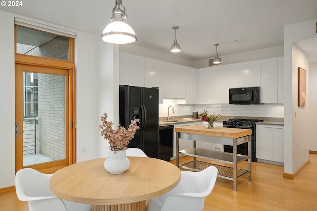 kitchen with pendant lighting, light wood-type flooring, white cabinetry, and black appliances